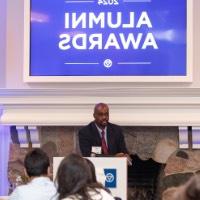 Quincy Williams speaking in microphone with 2024 Alumni Awards sign behind him